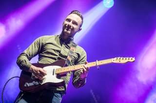 May be an image of 1 person, playing a musical instrument, standing, guitar and indoor