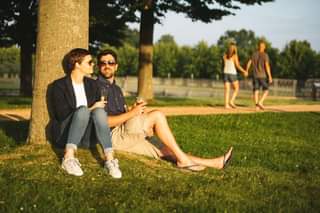 May be an image of 2 people, people sitting, grass and park